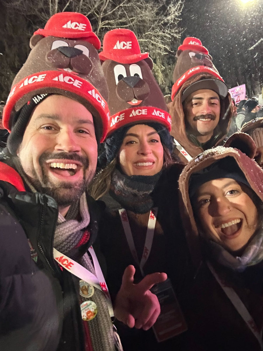 Four fans wearing custom Ace Hardware foam groundhog hats in the snow on Groundhog Day